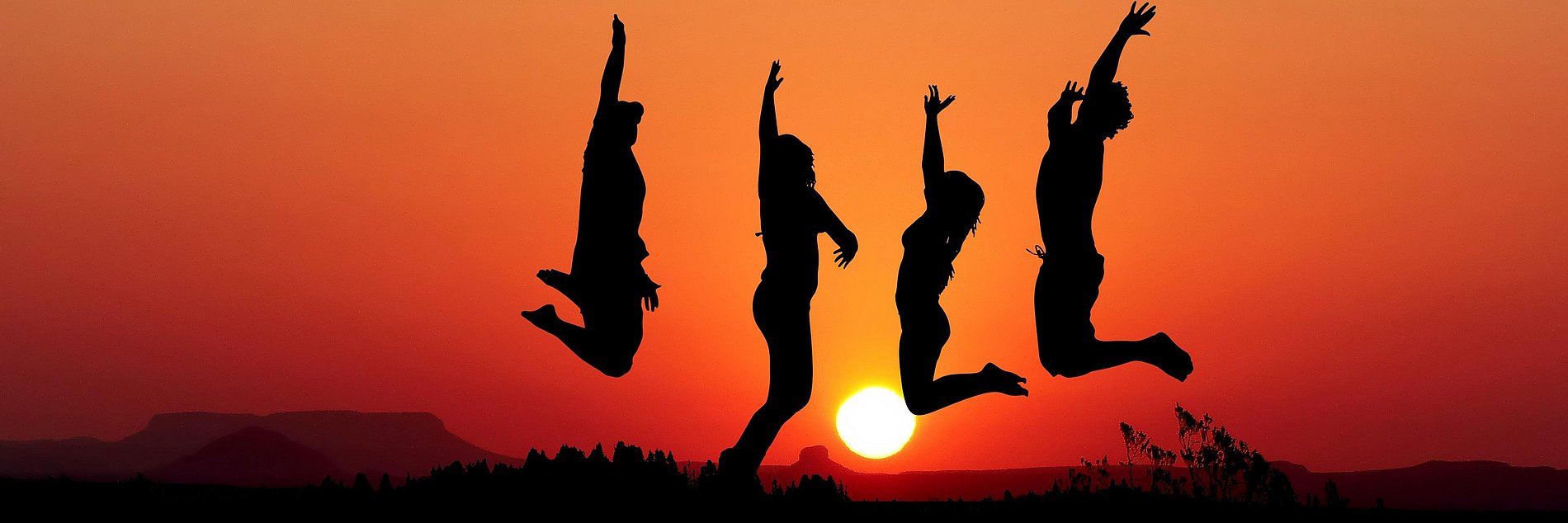 Silhouetten von 4 springenden Menschen vor einem Sonnenuntergang