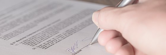 Eine Frauenhand unterschreibt einen Vertrag mit einem Kugelschreiber