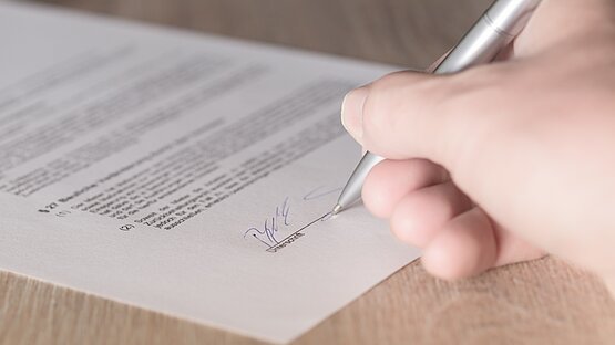 Eine Frauenhand unterschreibt einen Vertrag mit einem Kugelschreiber